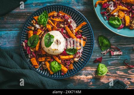 Insalata di radicchio con bastoncini di patate dolci arrostiti, noci e burrata su fondo rustico in legno blu, vista dall'alto Foto Stock