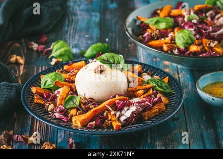 Insalata di radicchio con bastoncini di patate dolci arrostiti, noci e burrata su fondo rustico in legno blu Foto Stock