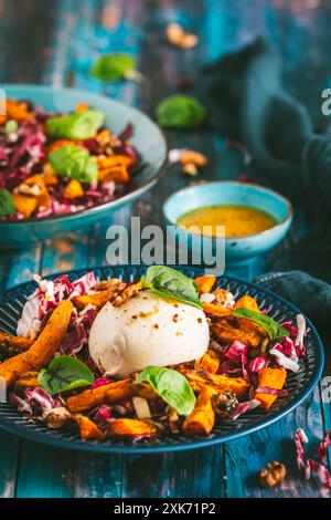 Insalata di radicchio con bastoncini di patate dolci arrostiti, noci e burrata su fondo rustico in legno blu, verticale Foto Stock