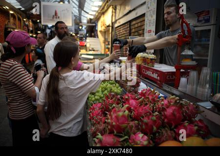 Le ragazze comprano succo di frutta da un venditore di un banco di frutta al mercato di Machane Yehuda dove vengono venduti anche frutta e uva del drago, ci sono anche altre persone. Foto Stock