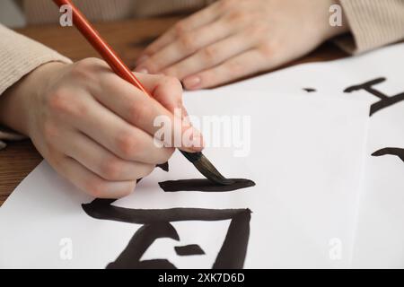 Calligrafia. Donna con pennello che scrive parola Bird in cinese su carta a tavola, primo piano Foto Stock