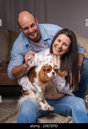 Famiglia felice con un cane. Una donna tiene tra le braccia il Cavalier King Charles Cocker Spaniel e ride allegramente, un uomo guarda con tenerezza l'animale Foto Stock