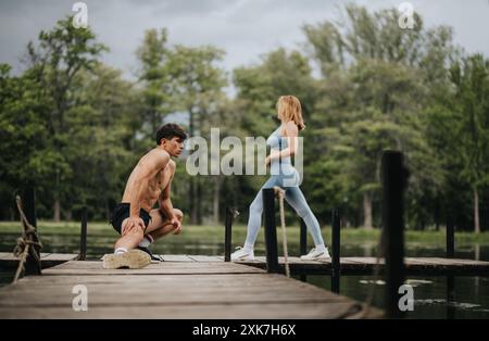 Coppia atletica che esegue esercizi all'aperto su un molo vicino al lago Foto Stock