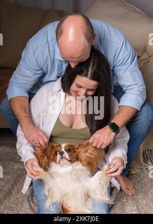 Famiglia felice con un cane. Una donna tiene tra le braccia il Cavalier King Charles Cocker Spaniel e ride allegramente, un uomo guarda con tenerezza l'animale Foto Stock