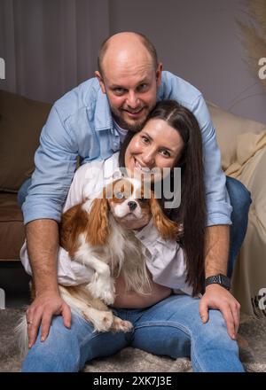 Famiglia felice con un cane. Una donna tiene tra le braccia il Cavalier King Charles Cocker Spaniel e ride allegramente, un uomo guarda con tenerezza l'animale Foto Stock
