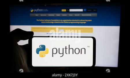 Persona che detiene un cellulare con il logo dell'organizzazione Python software Foundation (PSF) davanti alla pagina Web. Mettere a fuoco il display del telefono. Foto Stock