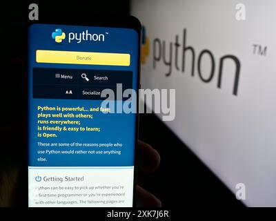 Persona che detiene un cellulare con la pagina Web dell'organizzazione Python software Foundation (PSF) davanti al logo. Messa a fuoco al centro del display del telefono. Foto Stock