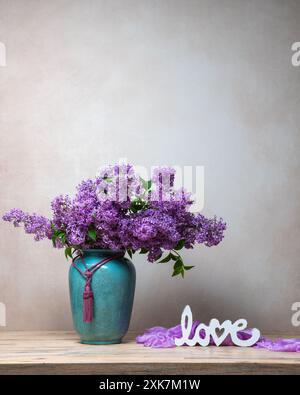 Natura morta con le lillas. Lilla in un grande vaso turchese su sfondo chiaro. L'iscrizione "amore". Copia spazio. Foto Stock