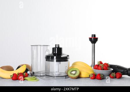 Kit frullatore a immersione, frutta fresca e fragole su un tavolo grigio su sfondo bianco Foto Stock