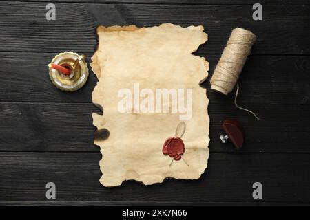 Foglio di vecchia carta pergamena con paraffina, spago e candela su un tavolo di legno nero, vista dall'alto Foto Stock