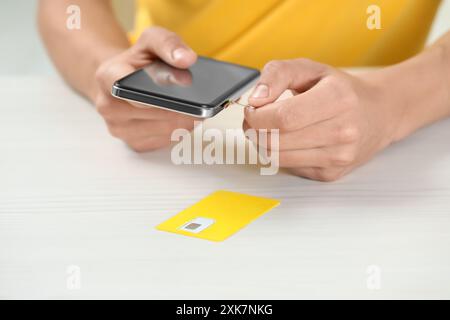 Uomo con vassoio per schede SIM con apertura espulsore nello smartphone, al tavolo di legno bianco, primo piano Foto Stock