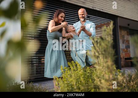 Ritratto di una famiglia felice che si diverte insieme all'aperto. Madre e padre che dondolano figlia, in piedi sulla terrazza. Foto Stock