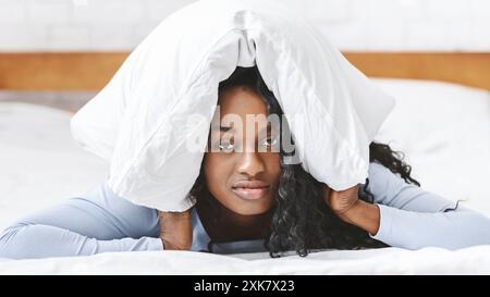 Giovane triste nero donna nel letto che copre la testa con il cuscino Foto Stock