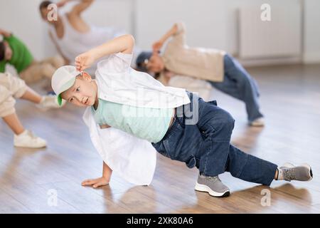 Ragazzi sportivi di dieci anni che allenano movimenti breakdance di danza vigorosa sulla pista durante la lezione di gruppo con insegnante maschile nella scuola di danza Foto Stock