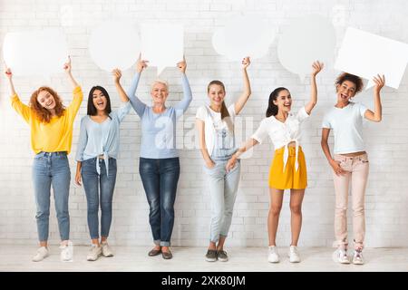 Ladies Holding vuoto Speech Bubbles in piedi su parete bianca in interni Foto Stock