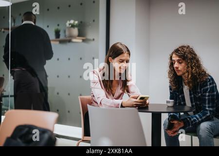 Giovani colleghi d'affari che utilizzano lo smartphone durante una pausa caffè in un ufficio moderno Foto Stock