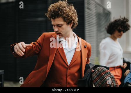 Giovane professionista con elegante tuta arancione che adatta la sua giacca all'aperto Foto Stock