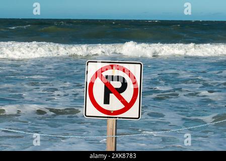 Un segno quadrato bianco con un cerchio rotondo rosso e la lettera p con vernice nera. La segnaletica e' su un palo di legno con l'oceano sullo sfondo. Foto Stock