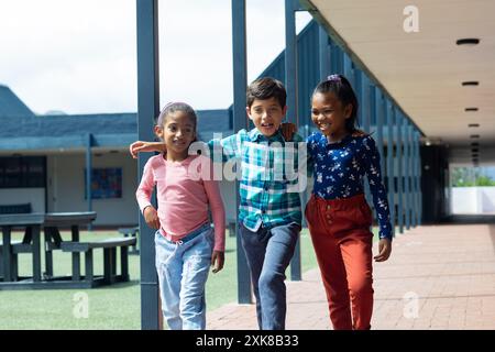 Tre bambini birazziali camminano insieme, sorridono, a scuola Foto Stock