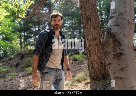 L'escursionista maschile esperto esplora il rigoglioso sentiero della foresta. L'avventuriero barbato in un abbigliamento casual gode di una passeggiata panoramica nel bosco. Lo stile di vita all'aperto e la natura sono collegati Foto Stock