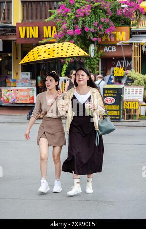 Due donne si godono una vacanza a piedi in un luogo turistico. I giovani turisti camminano per strada in un mercato nell'antica città di Hoi An Vietnam. Ragazza asiatica Foto Stock