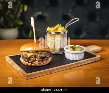 Delizioso hamburger a doppio manzo su ardesia nera con patatine fritte e sottaceti Foto Stock