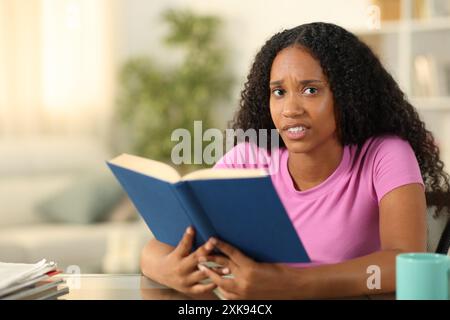 Una donna nera maledetta che legge un libro di carta ti guarda a casa Foto Stock