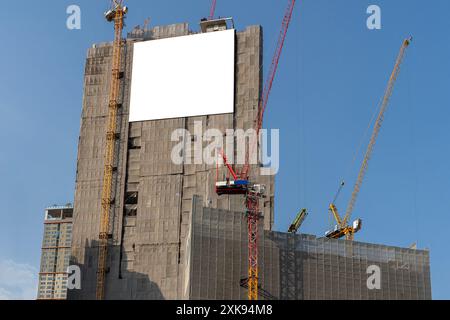 Tabellone informativo vuoto appeso sulle impalcature intorno al nuovo edificio in costruzione. Segnali di avvertimento in basso. Copia spazio. tracciato di ritaglio Foto Stock