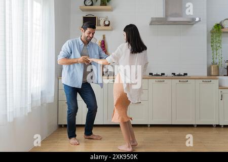 Coppia felice che si diverte in cucina ballando insieme per celebrare l'immigrazione o l'anniversario bel giovane marito che tiene per mano bella moglie mov Foto Stock