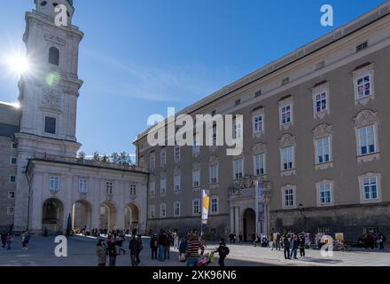 Salisburgo, Austria - 1 novembre 2023: Un'alta torre bianca con un orologio si erge di fronte ad un grande edificio grigio con molte finestre a Salisburgo, A. Foto Stock