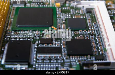 Primo piano dettagliato di una scheda a circuito stampato elettronica che mostra microchip, resistori e altri componenti, che rappresentano la tecnologia e l'hardware moderni. Foto Stock