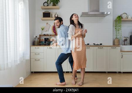 Felice marito e moglie millenari che ballano in cucina moderna celebrano l'anniversario del matrimonio a casa insieme, felice giovane coppia inquilini si divertono Foto Stock