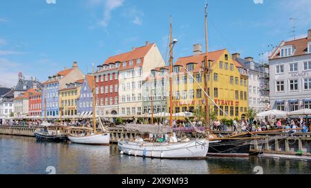 Copenaghen Danimarca 21 luglio 2024, Una giornata di sole a Nyhavn di Copenaghen, con edifici dai colori vivaci che costeggiano il lungomare. Le barche a vela sono attraccate e la gente passeggiava lungo le strade acciottolate. Foto Stock