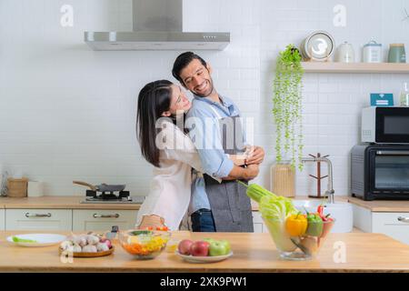 Una giovane coppia sorridente che cucina in cucina. Giocosa allegra giovane coppia birazziale che impastano insieme l'impasto sul bancone della cucina. Felice giovane coppia che cucina t Foto Stock