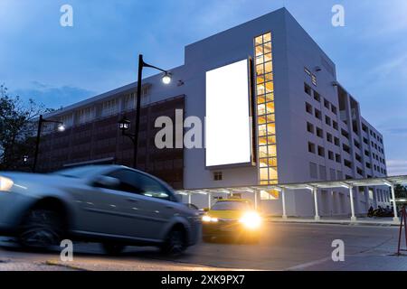 Lavagna bianca e alto edificio per affari di notte. Un luminoso cartellone bianco si distingue dalla zona del centro cittadino circostante la sera a. Foto Stock