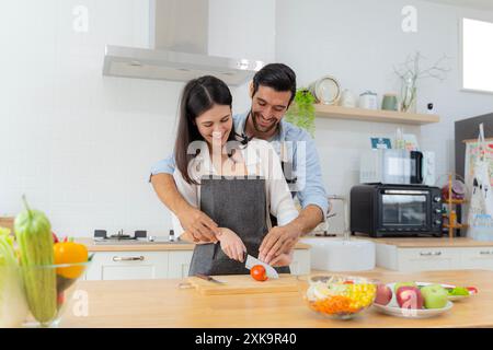 Una giovane coppia si diverte a preparare la colazione insieme in una bella mattinata, cucinare insieme, cucinare insieme, affettare i pomodori insieme. L Foto Stock