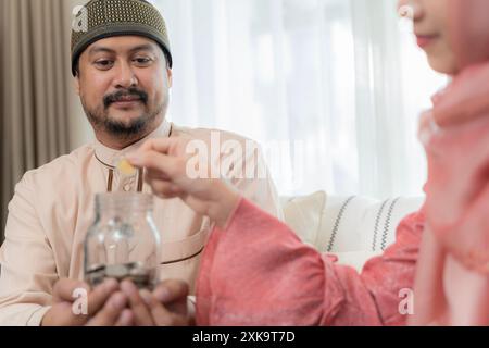 Risparmio sul concetto finanziario. Coppia musulmana con barattolo di monete. Mano di una donna che mette i soldi nel vaso di vetro etichettato tenuto da un uomo, risparmia e investe denaro Foto Stock