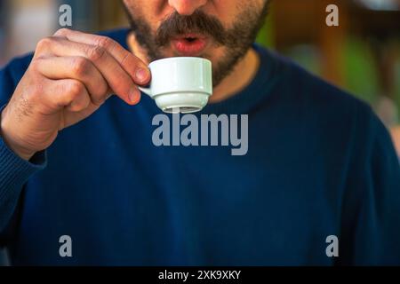 Una foto che cattura un uomo con una camicia blu gustando il tradizionale caffè turco servito in una tazza bianca, mostrando un delizioso momento culturale. Foto Stock