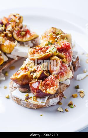 Toast a colazione con feta, fichi e pistacchi su un piatto bianco, sfondo bianco. Foto Stock