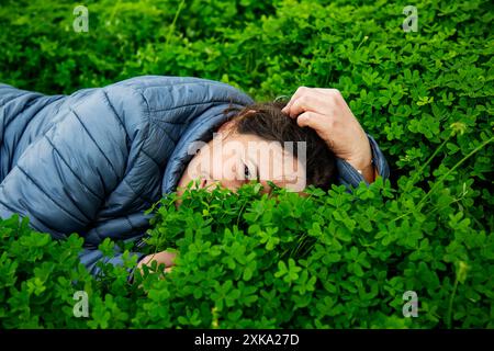 la donna giace sull'erba verde e nasconde la faccia a metà nel trifoglio Foto Stock