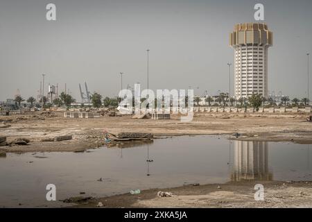 La costruzione del porto islamico di Jeddah e delle gru portuali si riflette nella pozzanghera nel cortile della spazzatura di Jeddah, la grande città dell'Arabia Saudita. Foto Stock