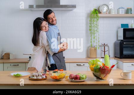 Una donna abbraccia felicemente un uomo, una coppia felice. Giovane coppia innamorata di divertirsi mentre preparano una colazione insieme in una bella mattinata. Cucinare, toge Foto Stock