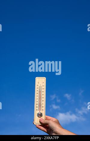 Termometro in legno che mostra temperature elevate in una giornata di sole con cielo blu e nuvole. Foto Stock