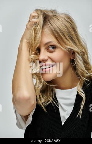 Una giovane donna dai capelli biondi trasuda eleganza con un pullover nero su sfondo grigio. Foto Stock