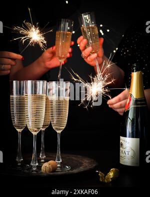 scena celebrativa con le mani che tengono scintillanti e flauti di champagne pieni di bollicine. lo sfondo scuro mette in risalto l'atmosfera festosa e scintillante. Foto Stock