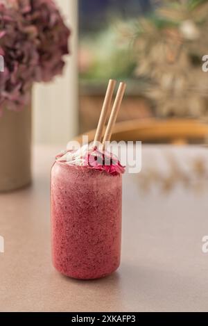 Frullato vegano di frutta rossa decorato con noci di cocco e fiori commestibili su un tavolo da caffetteria. Vista laterale. Foto Stock
