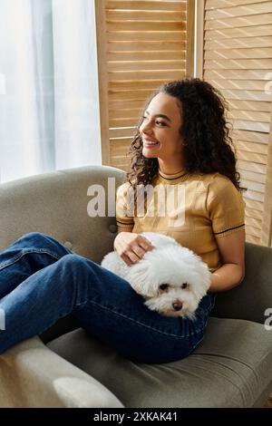 Una donna si rilassa su un divano mentre tiene delicatamente la sua soffice frise bianca. Foto Stock