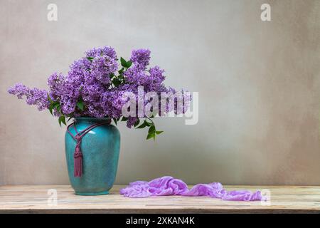 natura morta con un enorme bouquet di fiori lilla in un grande vaso turchese su uno sfondo chiaro, con uno scialle lilla adagiato accanto ad esso. Copia spazio Foto Stock