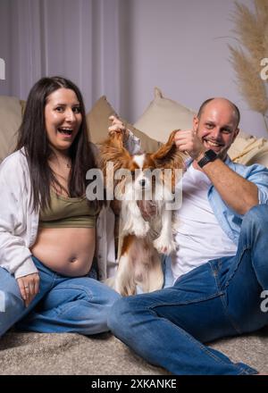 Una famiglia che aspetta un bambino si diverte con il suo cane, un cocker spaniel. Ridono e giocano allegramente. Cavalier King Charles Cocker Spaniel Foto Stock