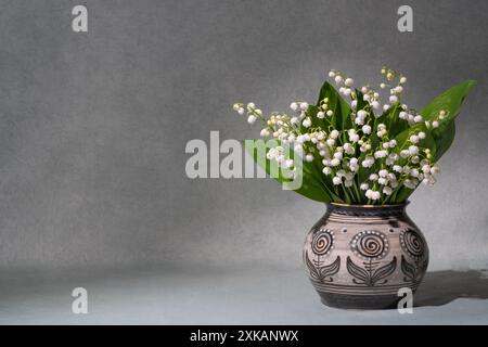 Un piccolo bouquet di freschi fiori primaverili. Gigli della valle in un vaso chiaro isolato su sfondo grigio. Molto spazio per il testo. natura morta, postco Foto Stock